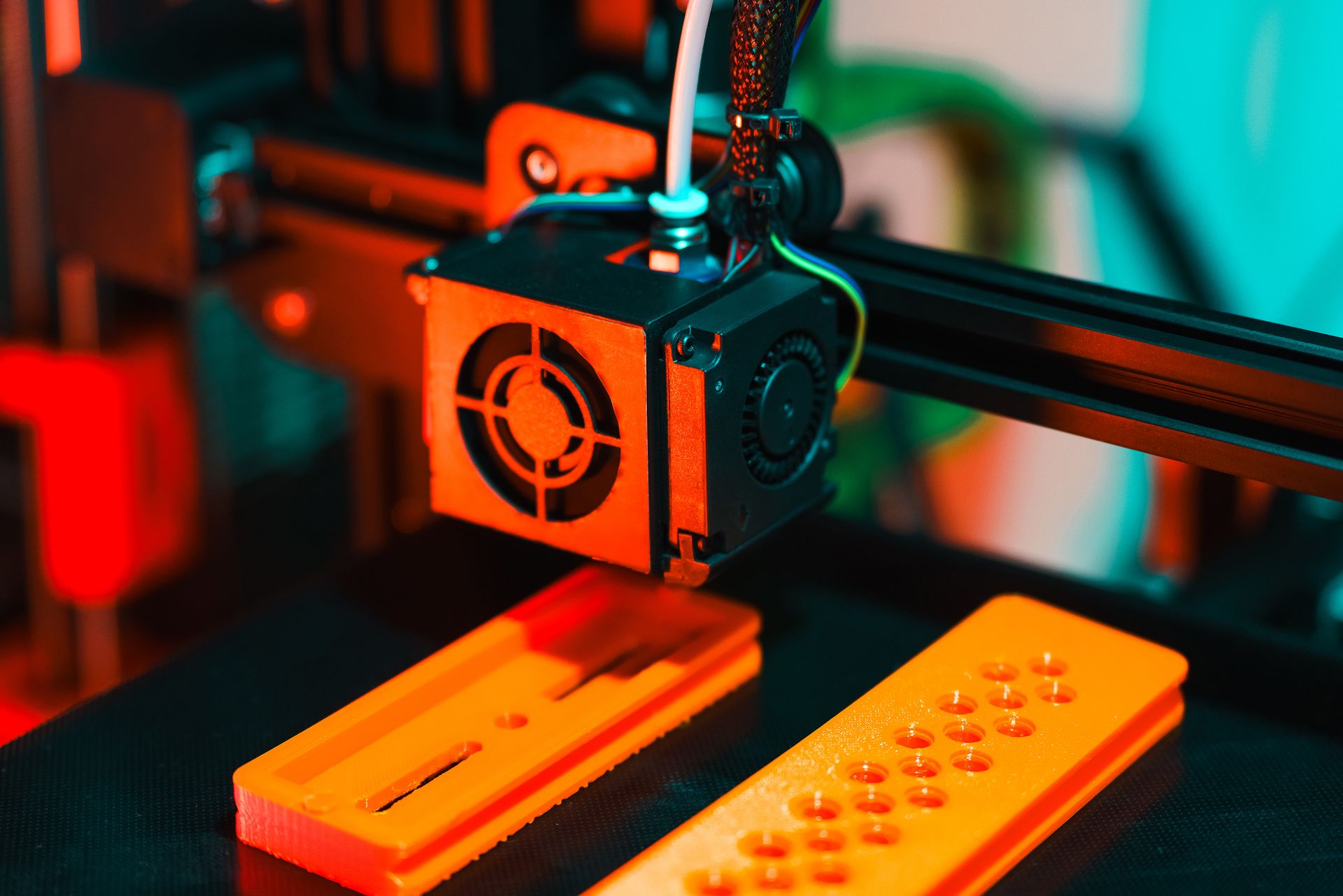 Cabeça de uma impressora 3D sobre duas peças impressas em PLA laranja